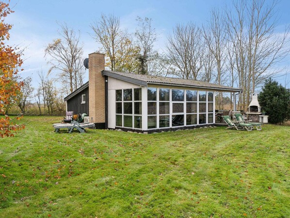 Ein modernes Haus mit einer großen Glasfront, einem Backstein-Schornstein und einer Terrasse mit Gartenmöbeln.