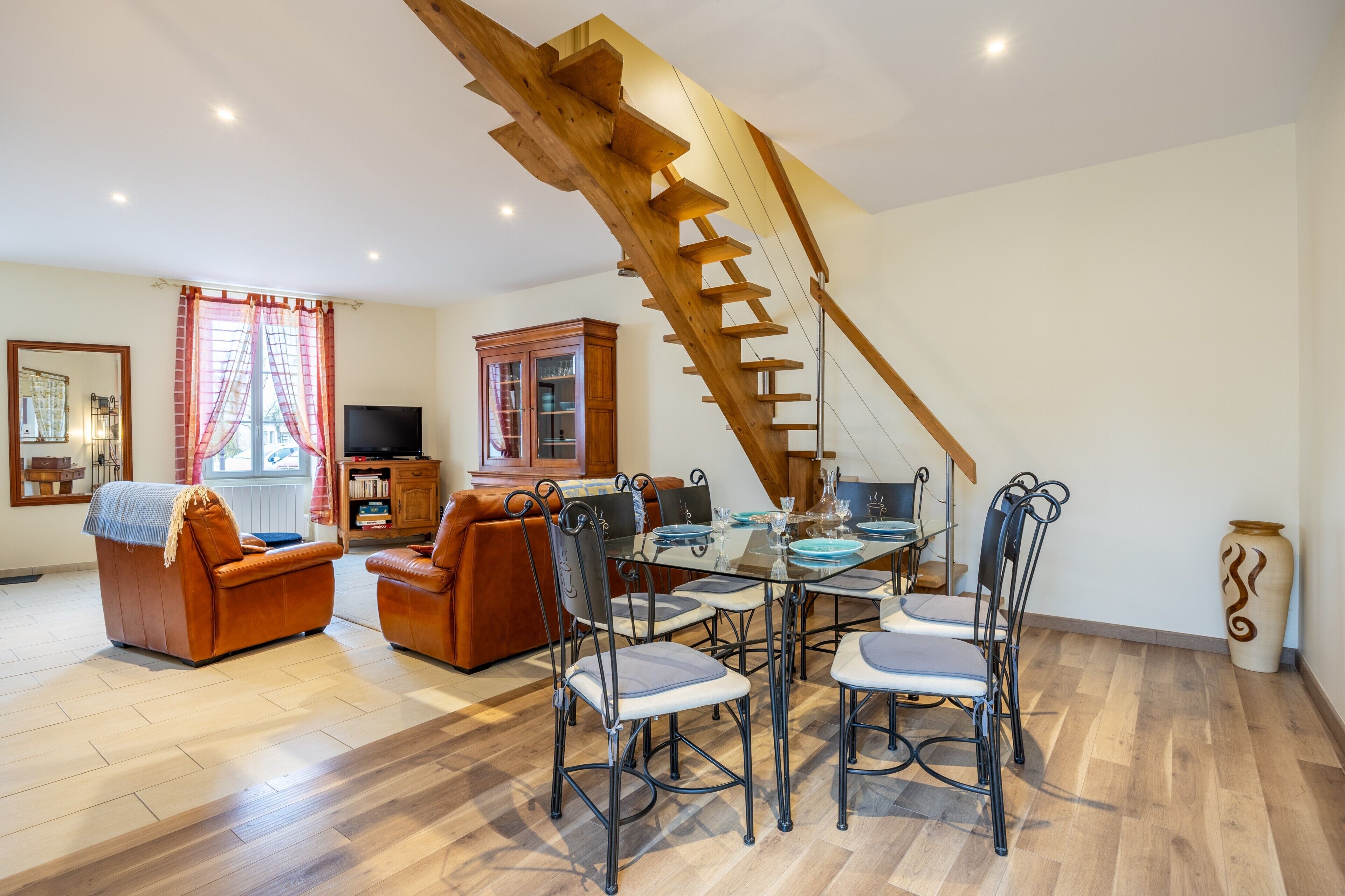 Un espace repas agrémenté d’un escalier en bois, de canapés en cuir et d’une table en verre.