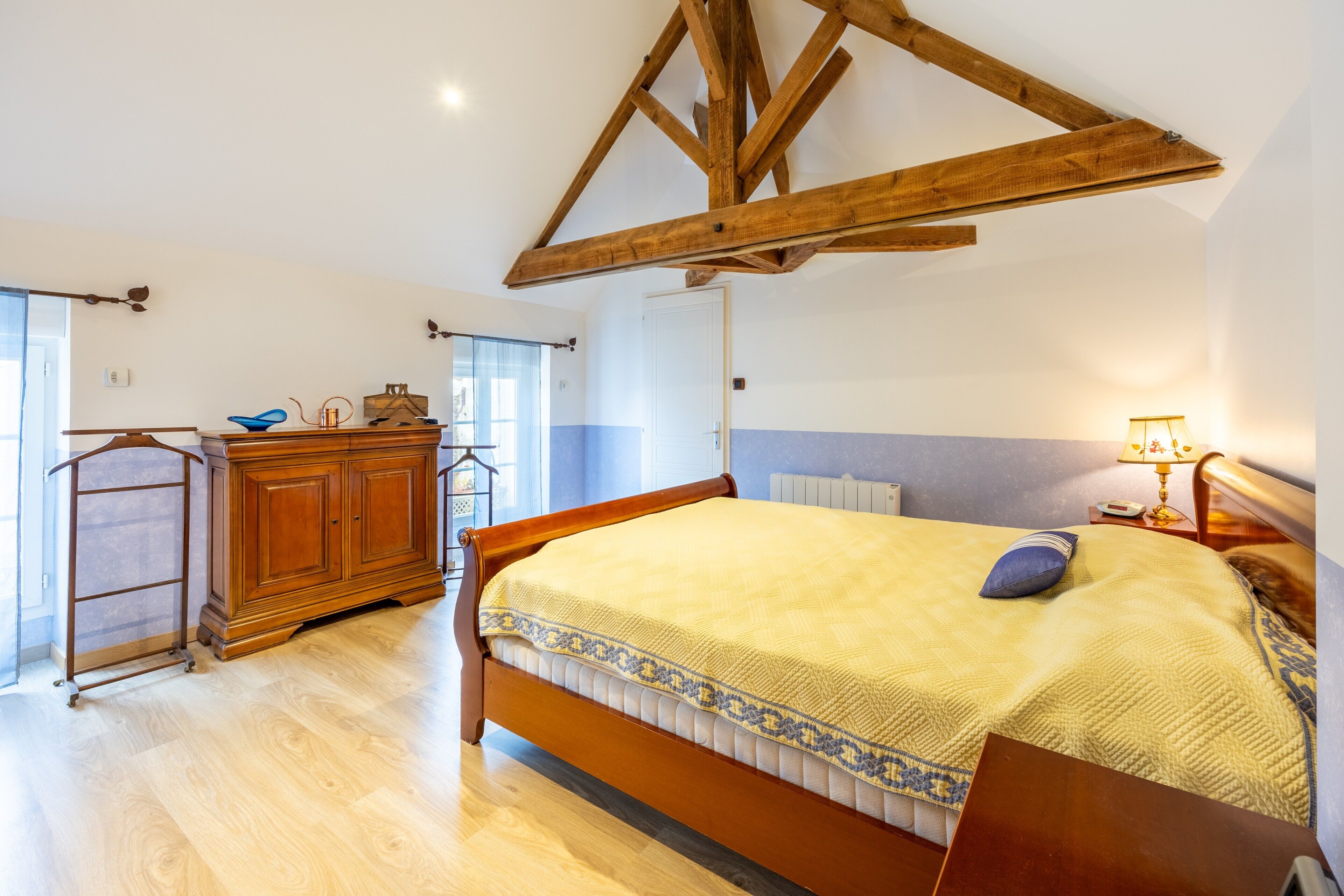 Une chambre à coucher avec un lit en bois, une commode, un radiateur et une fenêtre avec des rideaux.