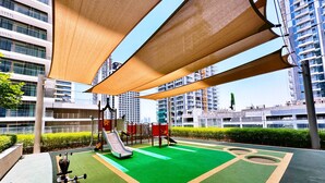 Un terrain de jeux extérieur doté d’un toboggan, de structures d’escalade et d’appareils de musculation, le tout entouré d’immeubles de grande hauteur.