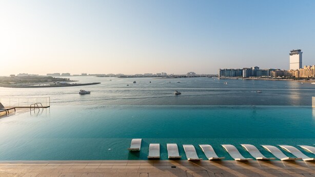 Une piscine à débordement située au bord de l’eau, dotée de chaises longues, offrant une vue dégagée sur la mer et, en arrière-plan, un panorama sur la ville.