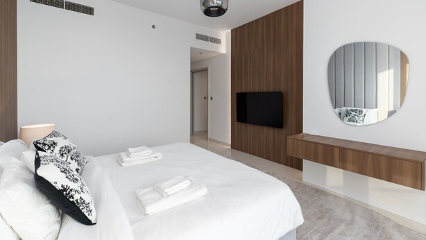 Ein modernes Hotelzimmer mit einem großen Bett, einem Flachbildfernseher, einem runden Spiegel und einer Wandpaneele aus Holz.