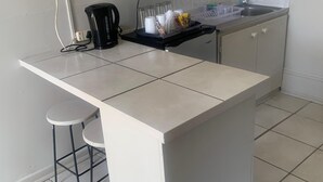 Eine kleine Küche mit weißer Arbeitsplatte, einer Mikrowelle, einem Wasserkocher und einem Spülbecken.
