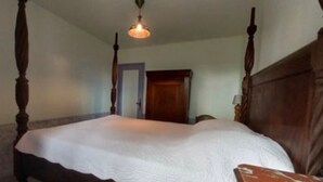 A four-poster bed with a wooden headboard, a hanging light fixture, and a door in the background. - Gîte du Moulin de Chanvre with Private Terrace and Garden (Preuilly-sur-Claise)