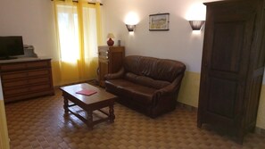 A living room with a brown leather sofa, a wooden coffee table, a wooden cabinet, and a television on a stand.