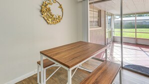 A dining area with a wooden table and bench, a decorative leaf wreath on the wall, and a sliding glass door leading to a patio with a view of a yard. - Gateway to Orlando Theme Parks! Home w/ Large Yard (Winter Park)