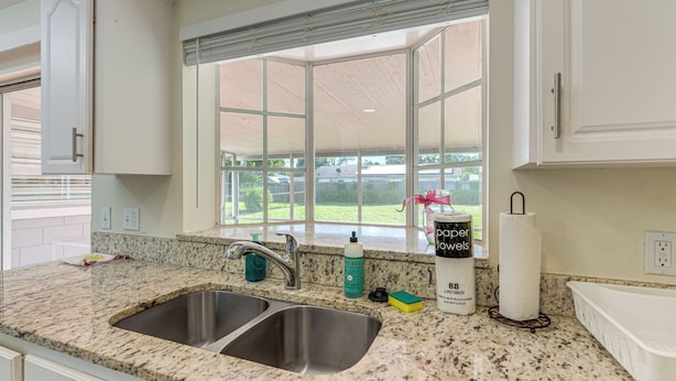 A kitchen with granite countertops, stainless steel sinks, and a window overlooking a backyard. - Gateway to Orlando Theme Parks! Home w/ Large Yard (Winter Park)