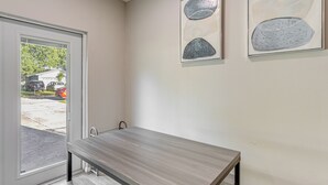 A modern room with a wooden table and benches, a sliding glass door leading outside, and abstract wall art. - Townhome w/ Fenced Yard in Orlando Suburbs! (Winter Park)