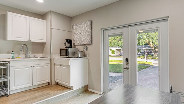 A modern kitchen with white cabinets, a stainless steel sink, and a microwave. There is a large window with a view of a green lawn and parked cars outside. - Townhome w/ Fenced Yard in Orlando Suburbs! (Winter Park)