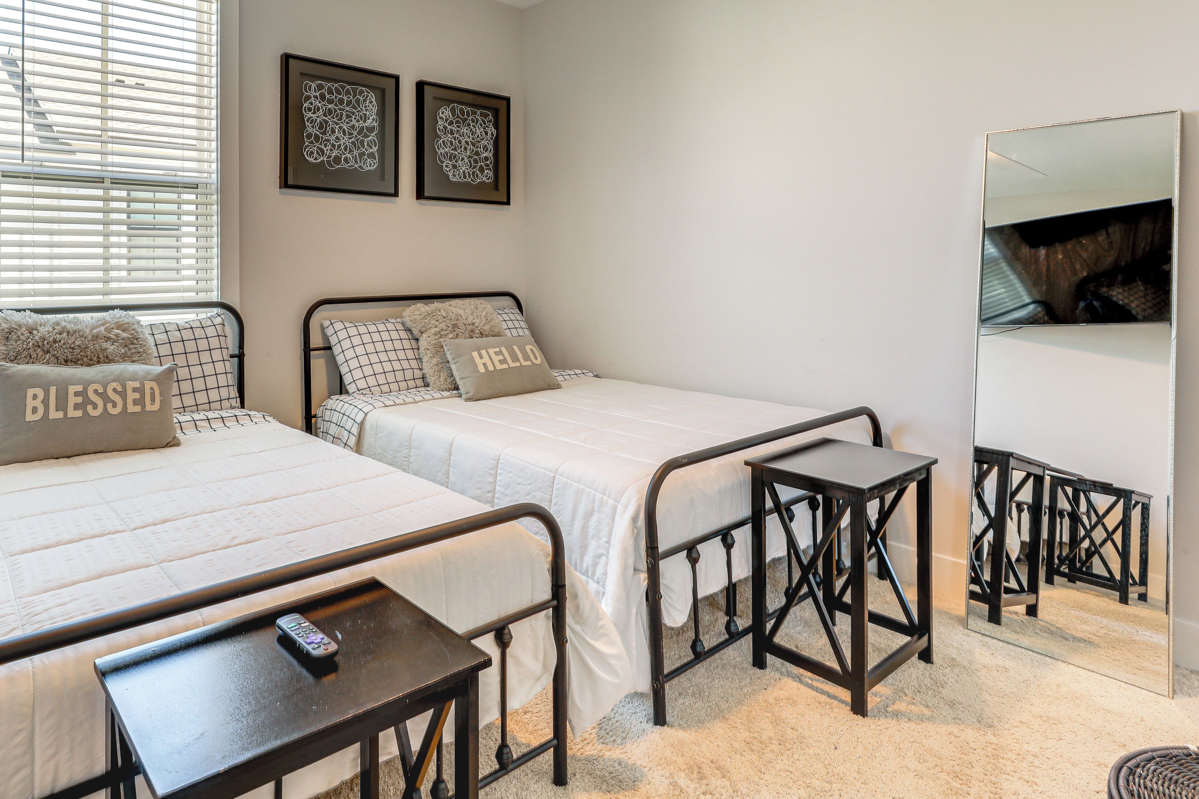 A bedroom with two beds, a bedside table, a mirror, and artwork on the wall.