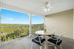 A covered balcony with a round table and chairs, a ceiling fan, and a view of a forested landscape. - Ozarks Vista Retreat 6ppl Stay (Kimberling City)