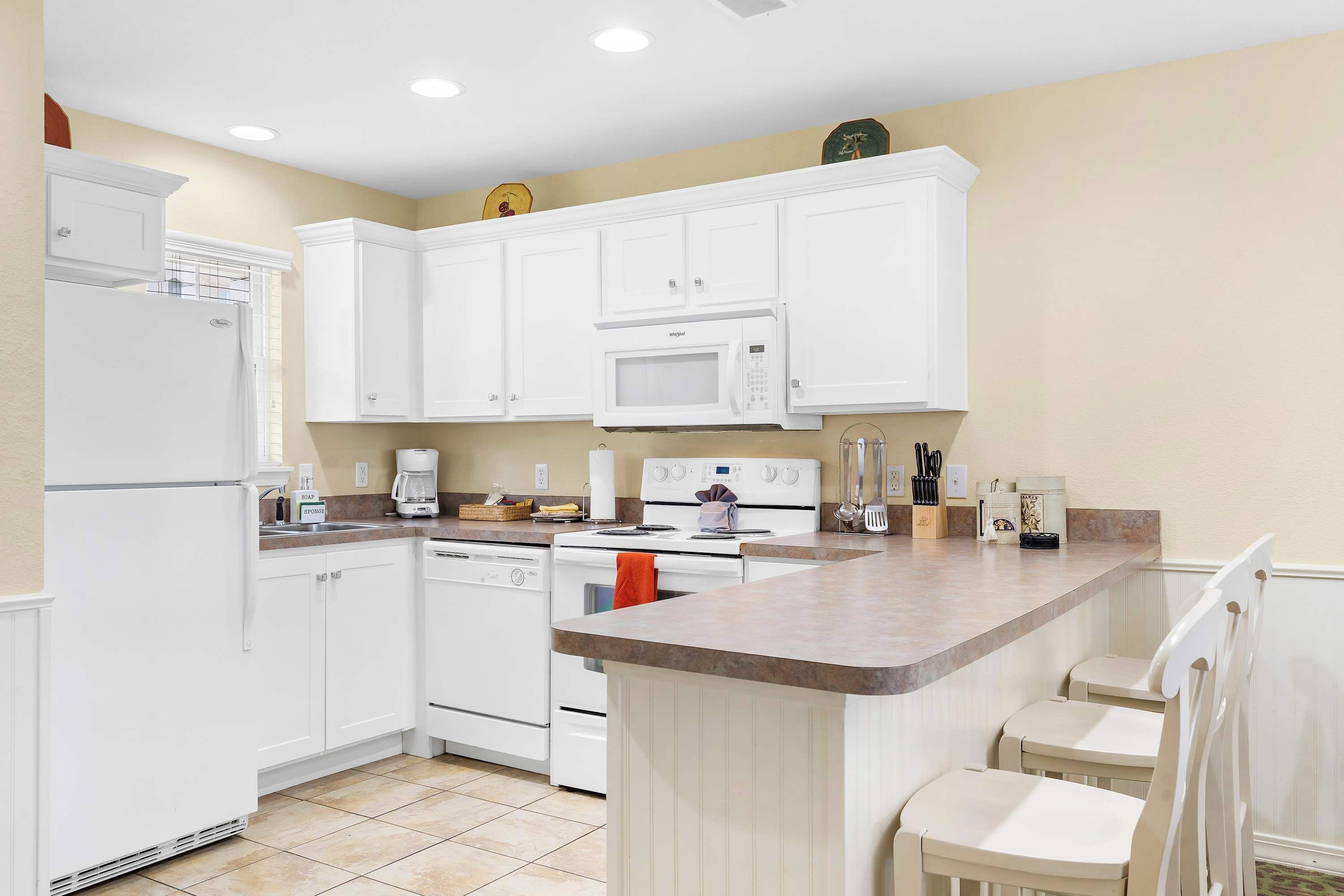 A modern kitchen with white cabinetry, a built-in microwave, a stove, and a coffee maker.