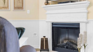 A living room with a fireplace, a television on top, and two framed botanical prints on the wall. - Ozarks Vista Retreat 6ppl Stay (Kimberling City)