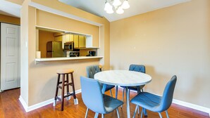 Un comedor con una mesa redonda y cuatro sillas, una cocina con microondas y refrigerador, y una puerta que da a otra habitación.