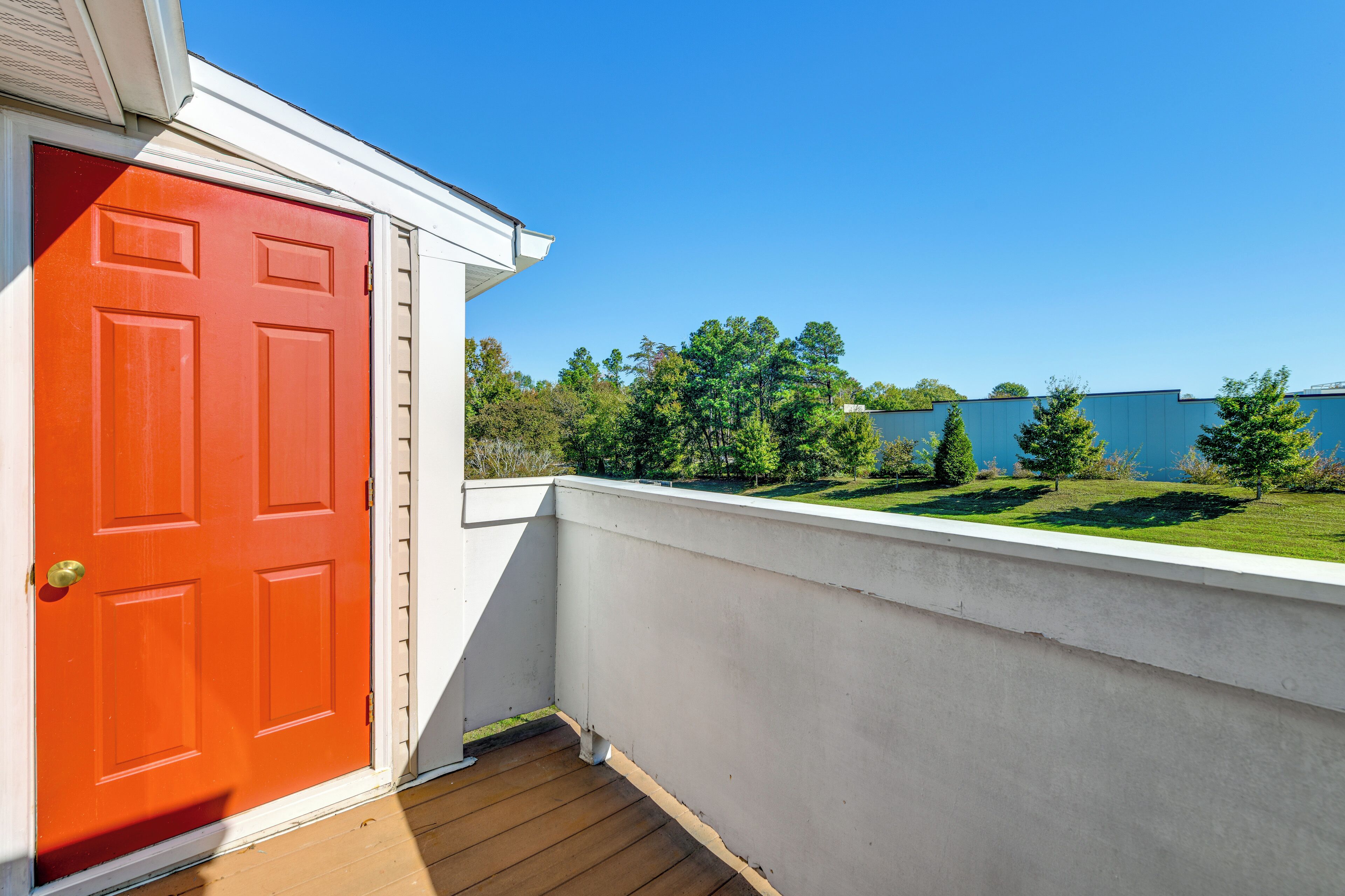 A red door on a balcony with a view of a green lawn and trees.