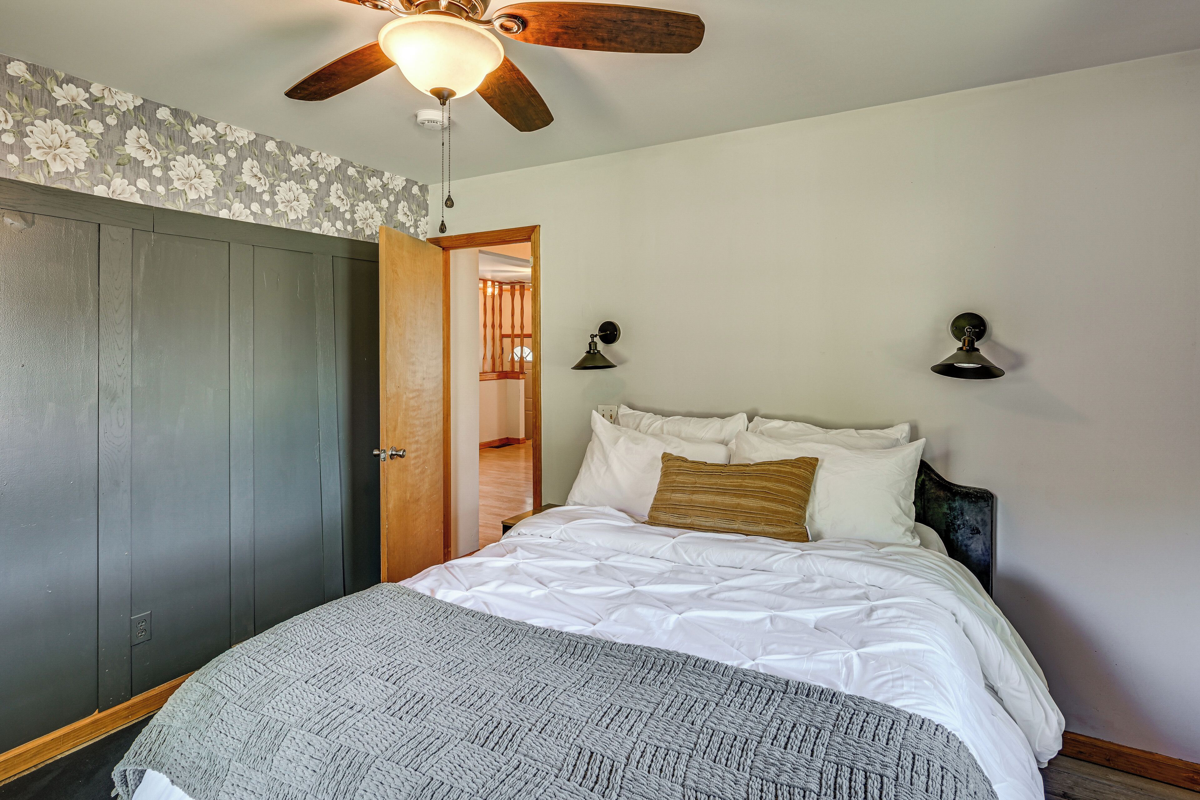 Quarto com cama, ventoinha no teto, guarda-roupa e porta que dá para outro cômodo.