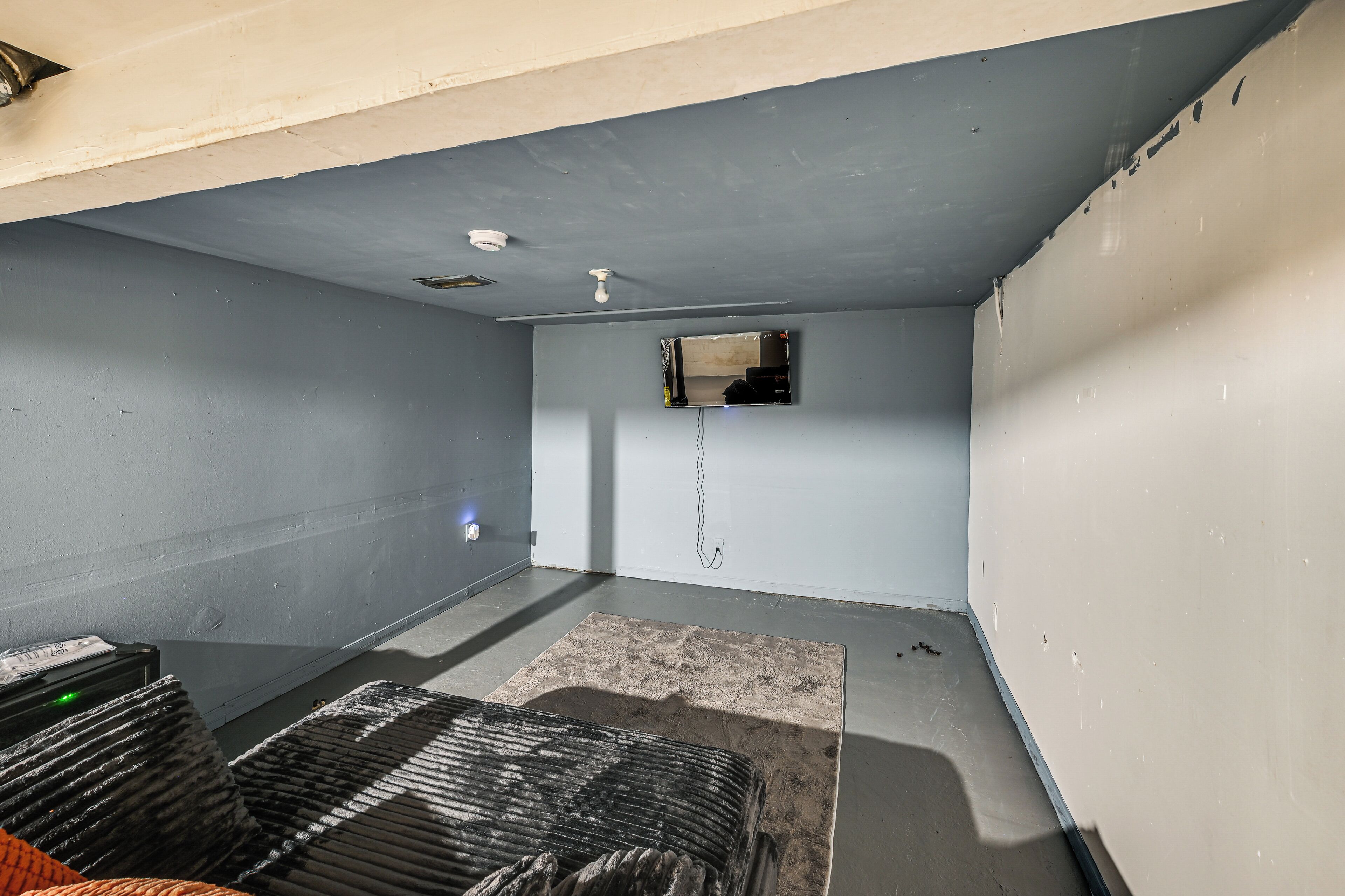 A room with a concrete floor, a small window, and a ceiling light fixture.