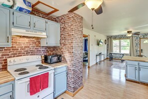 A kitchen with a brick wall, white cabinets, a stove, and a microwave. - 4 Mi to Lake Michigan: Updated Benton Harbor Home! (Benton Harbor)