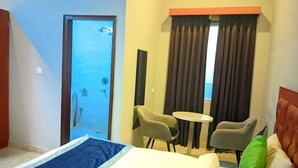 A hotel room with a bed, two chairs, a small table, a window with curtains, and a door leading to a bathroom. - Hotel Expo Mart Inn Behind India Expo (Greater Noida)