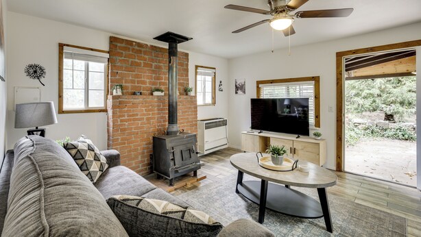 A living room with a brick fireplace, a ceiling fan, a TV, and a large window. - Modern Backcountry Retreat! Bike & Hike Mt Laguna (Mount Laguna)