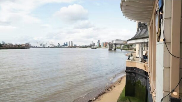 Vista sul fiume con un edificio in stile architettonico tradizionale, un ponte sullo sfondo e il profilo della città.