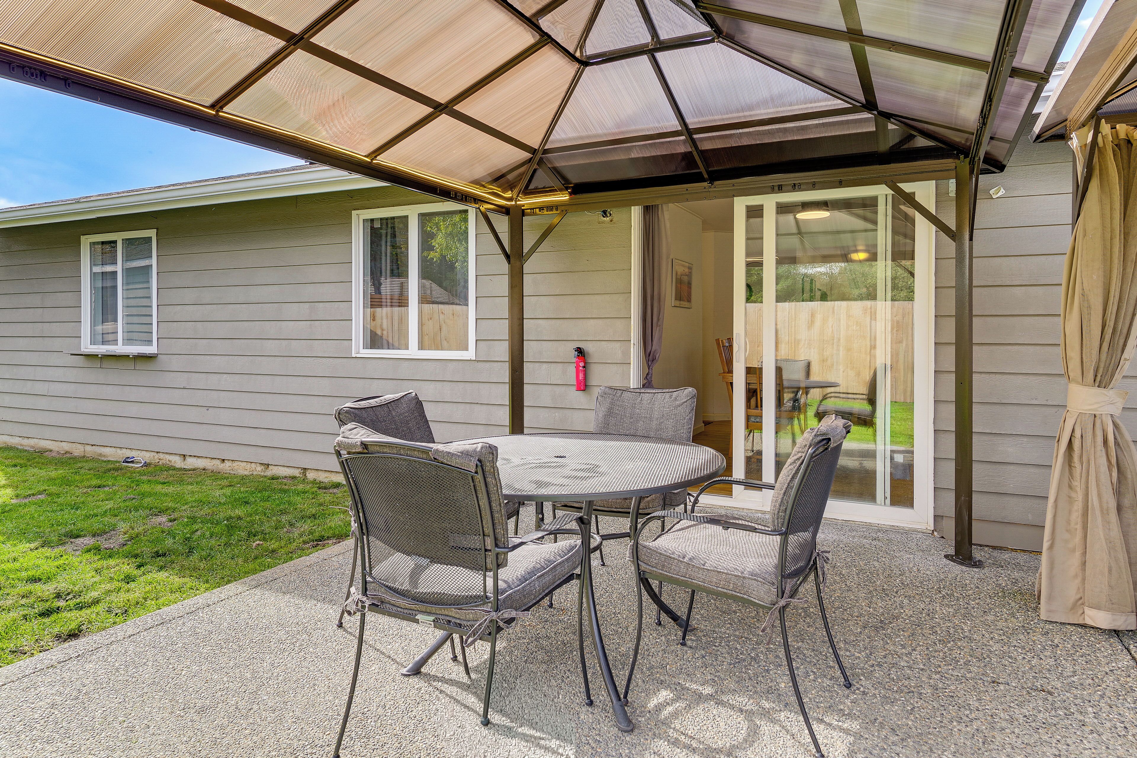 An outdoor patio with a covered table and chairs, a sliding glass door, and a grassy yard.