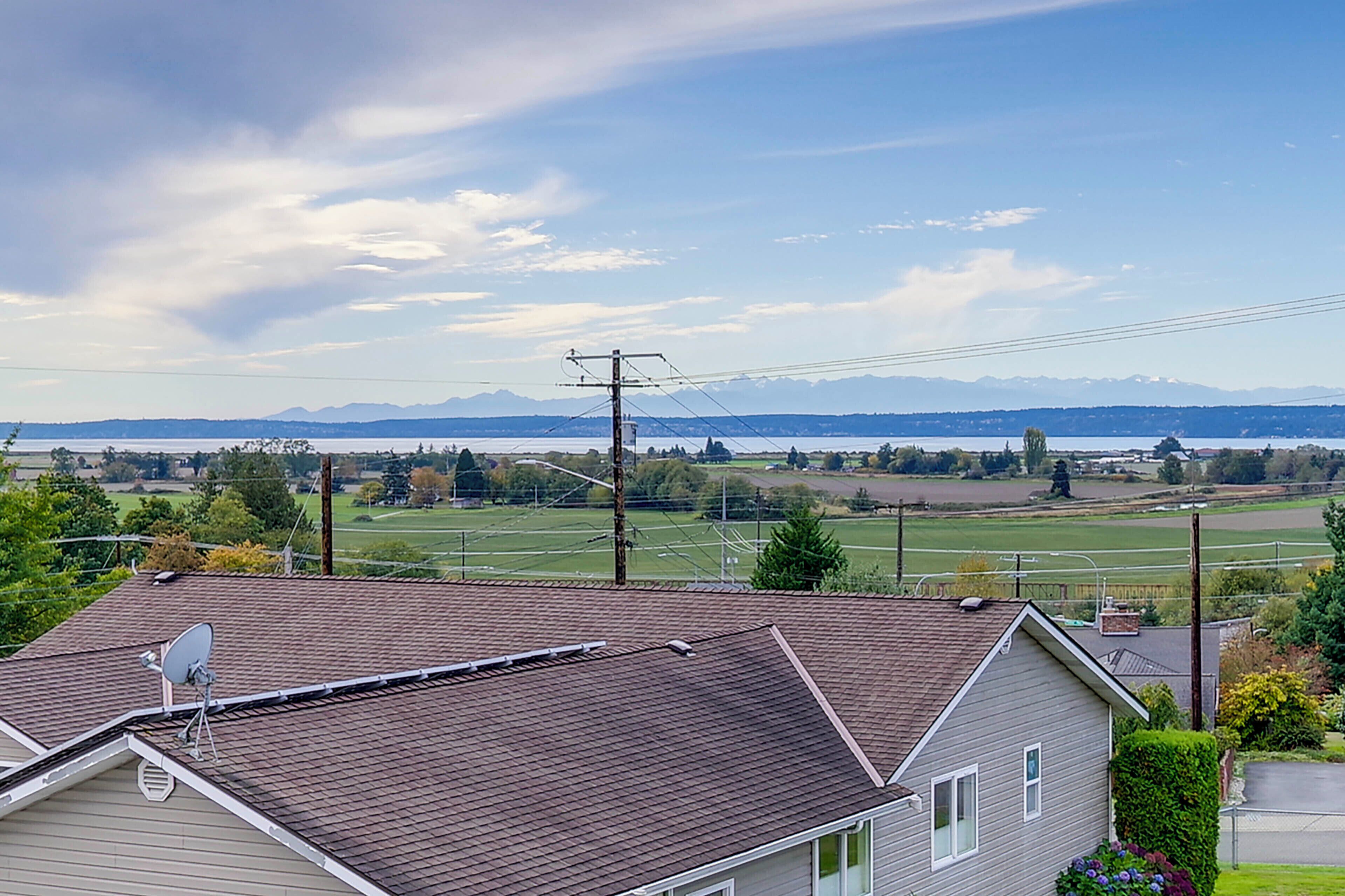 A house with a satellite dish on the roof, overlooking a green field and a body of water with mountains in the distance.