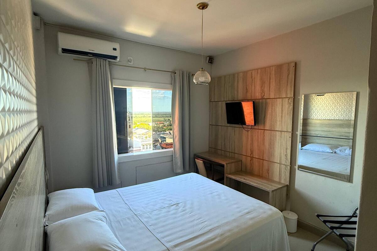 A hotel room with a bed, a desk, a TV, and a window with a view.