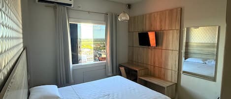A hotel room with a bed, a desk, a TV, and a window with a view.