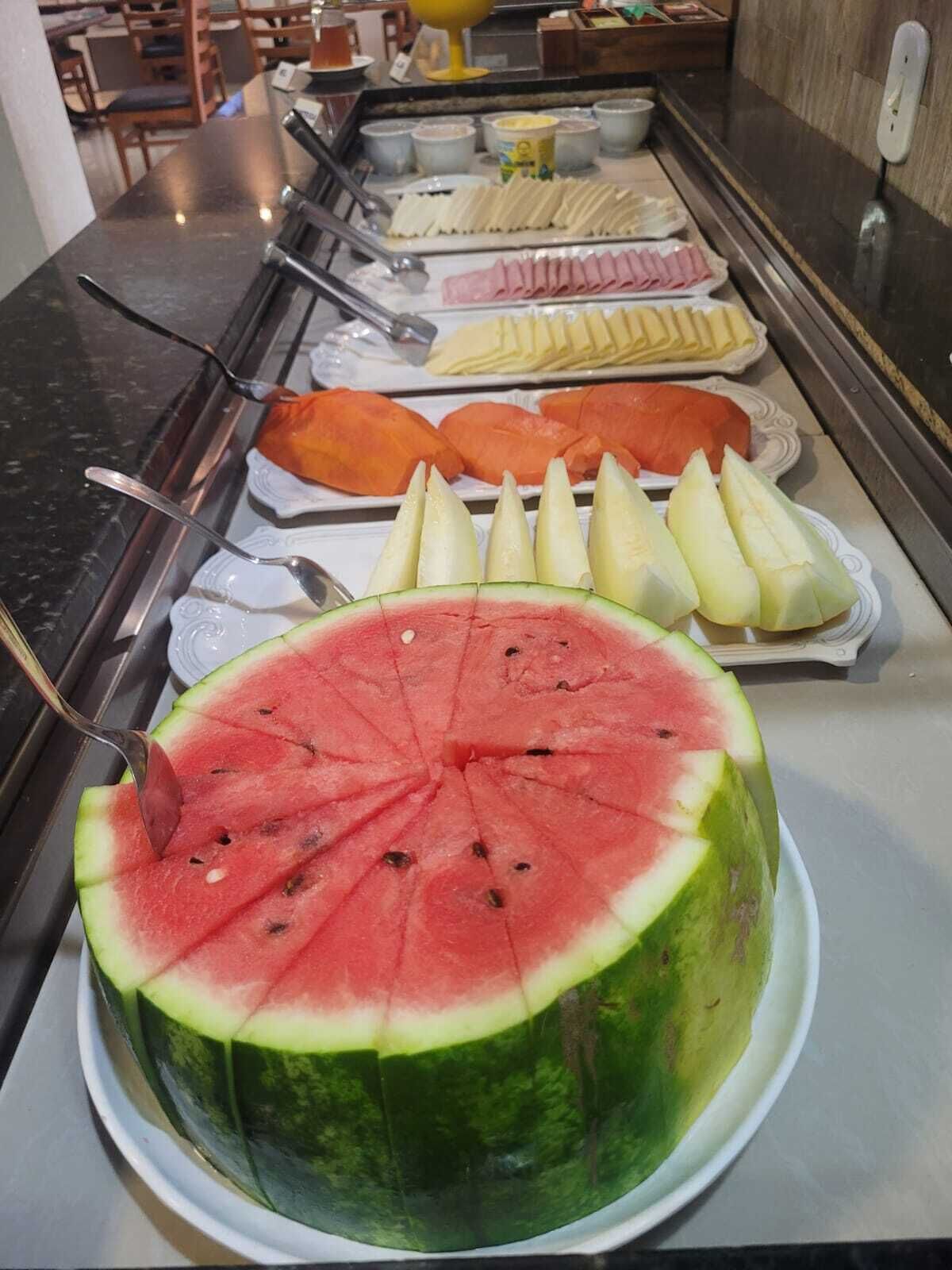 A buffet with a variety of food items including a large watermelon, sliced fruits, and other dishes.