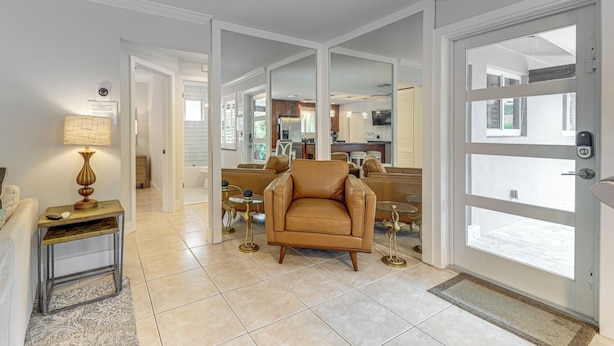 A spacious living area with a leather armchair, a small side table with a lamp, and a view into the kitchen through a glass door. - Walkable Island City Oasis w/ Private Heated Pool! (Wilton Manors)