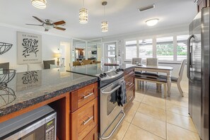 A modern kitchen with a granite countertop, stainless steel appliances, wooden cabinets, and a dining area with a table and chairs. - Walkable Island City Oasis w/ Private Heated Pool! (Wilton Manors)