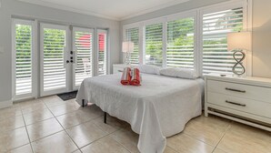 A bedroom with a large bed, white curtains, a nightstand, and a lamp. - Walkable Island City Oasis w/ Private Heated Pool! (Wilton Manors)