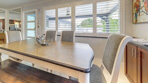 A dining area with a wooden table, cushioned chairs, and a view of the outdoors through large windows. - Walkable Island City Oasis w/ Private Heated Pool! (Wilton Manors)