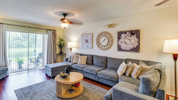 A modern living room with a grey sofa, a round coffee table, and a large window with curtains. - Pool & Hot Tub Access at Resort Home in Poinciana (Kissimmee)