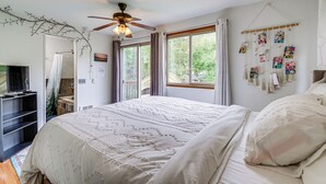 Une chambre à coucher avec un lit, un ventilateur de plafond, une fenêtre avec des rideaux et un mur décoré de tableaux.