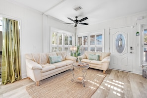 A spacious living room with two cream-colored sofas, a woven coffee table, and a ceiling fan. - Steps to Ocean! PCB Family Home w/ Outdoor Oasis (Panama City Beach)