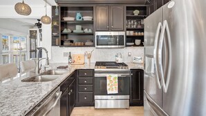 A modern kitchen with dark cabinetry, stainless steel appliances, a marble countertop, and a chandelier. - Steps to Ocean! PCB Family Home w/ Outdoor Oasis (Panama City Beach)