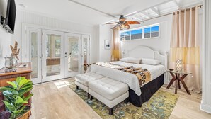 A bedroom with a bed, a ceiling fan, a bedside table, a floor lamp, and a large window. - Steps to Ocean! PCB Family Home w/ Outdoor Oasis (Panama City Beach)