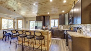 A spacious kitchen with wooden cabinets, a central island with bar stools, and a large window providing natural light. - Big Bear Mtn Fun: Family Cabin w/ Game Room (Sugarloaf)