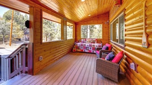 A log cabin with a wooden deck, a sofa with cushions, and a large window. - Big Bear Mtn Fun: Family Cabin w/ Game Room (Sugarloaf)