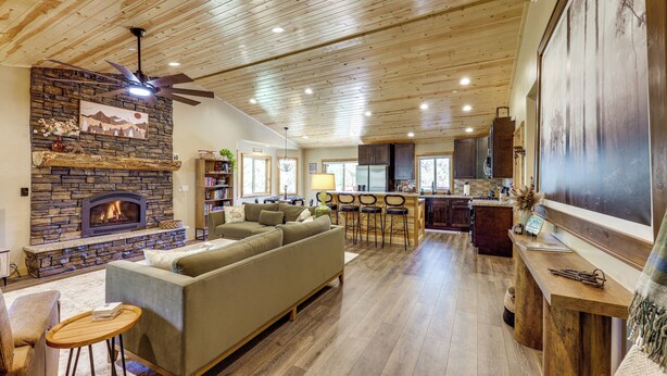 A spacious living room with a stone fireplace, a sofa, and a dining area with bar stools. - Big Bear Mtn Fun: Family Cabin w/ Game Room (Sugarloaf)