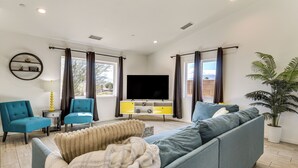 Una sala de estar moderna con un sofá, dos sillones, un televisor y una planta grande en maceta.