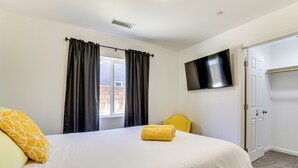 Una habitación de hotel con cama, televisor montado en la pared, ventana con cortinas y puerta.