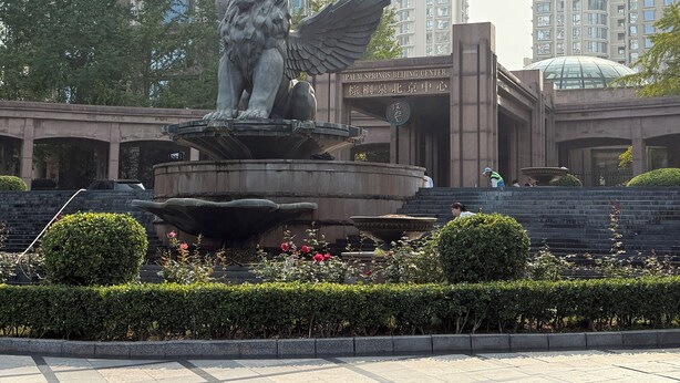 Una estatua de león de piedra con alas, una fuente y un edificio con un letrero que dice "Palm Springs Beijing Center".