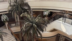 Ein mehrgeschossiges Atrium mit Marmortreppen, Palmen und einer zentralen Sitzgruppe mit einem Blumenstrauß.