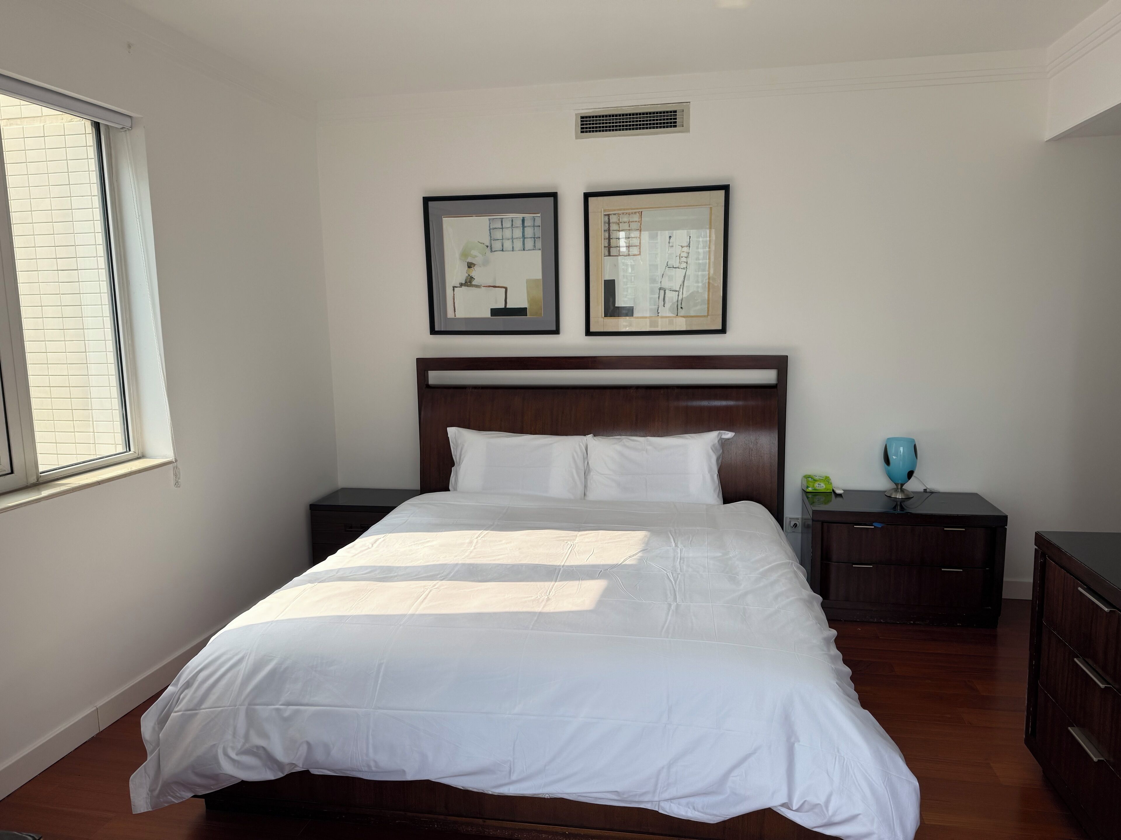 A neatly made bed with white linens, a wooden headboard, and two bedside tables with lamps.