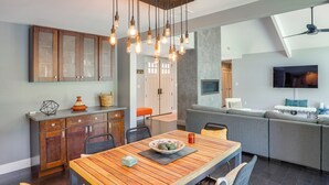 A modern kitchen with wooden cabinets, a dining table with chairs, and a built-in seating area with a TV.