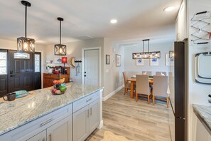 A modern kitchen with granite countertops, pendant lighting, a dining area with a wooden table and chairs, and a refrigerator. - North Fort Myers Waterfront Home w/ Pool & Dock (North Fort Myers)