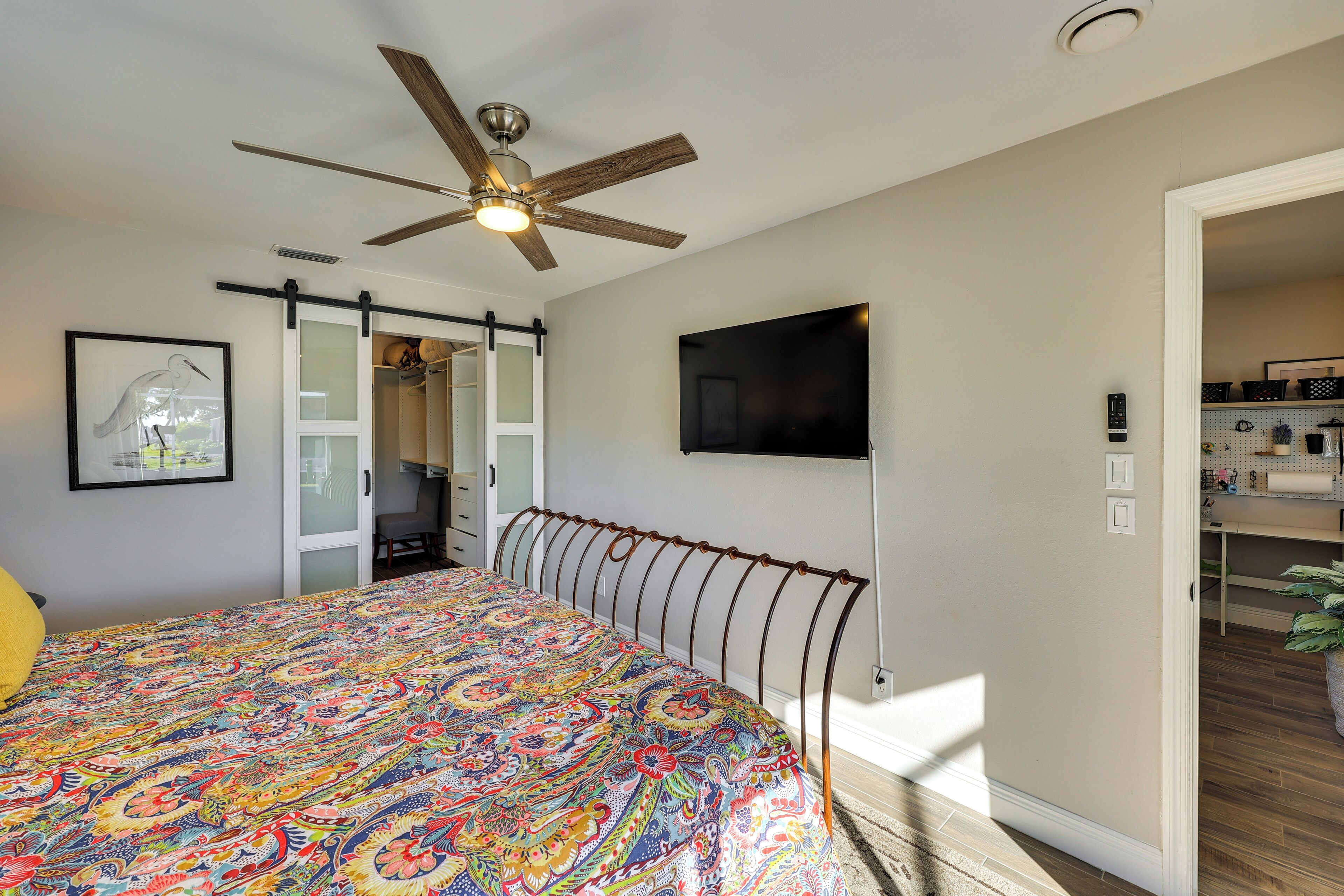 A bedroom with a bed, a ceiling fan, a sliding door closet, a mounted TV, and a visible kitchen area.